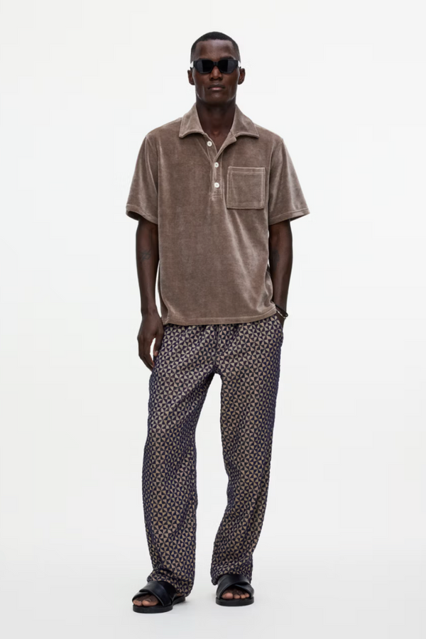 Man wearing a brown textured shirt and patterned pants on a white background