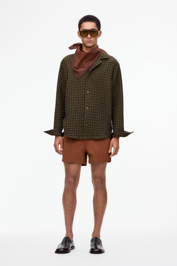 Man wearing a patterned shirt, brown shorts, and sunglasses on a white background